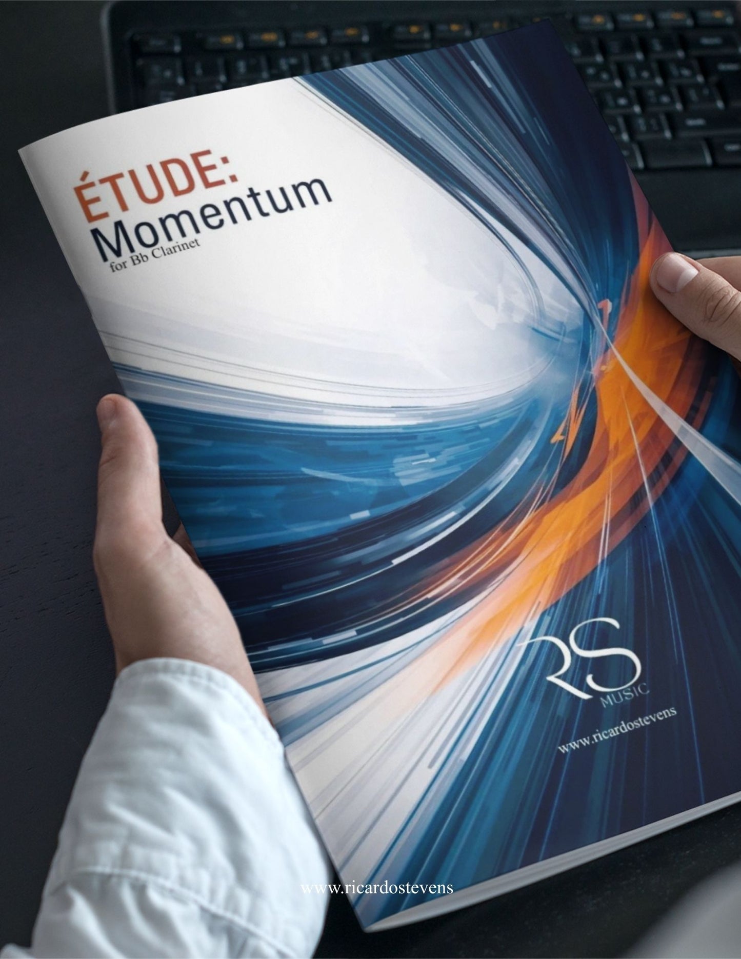 Book titled 'Étude: Momentum' held by a person with a blurred keyboard in the background by Ricardo Stevens.
