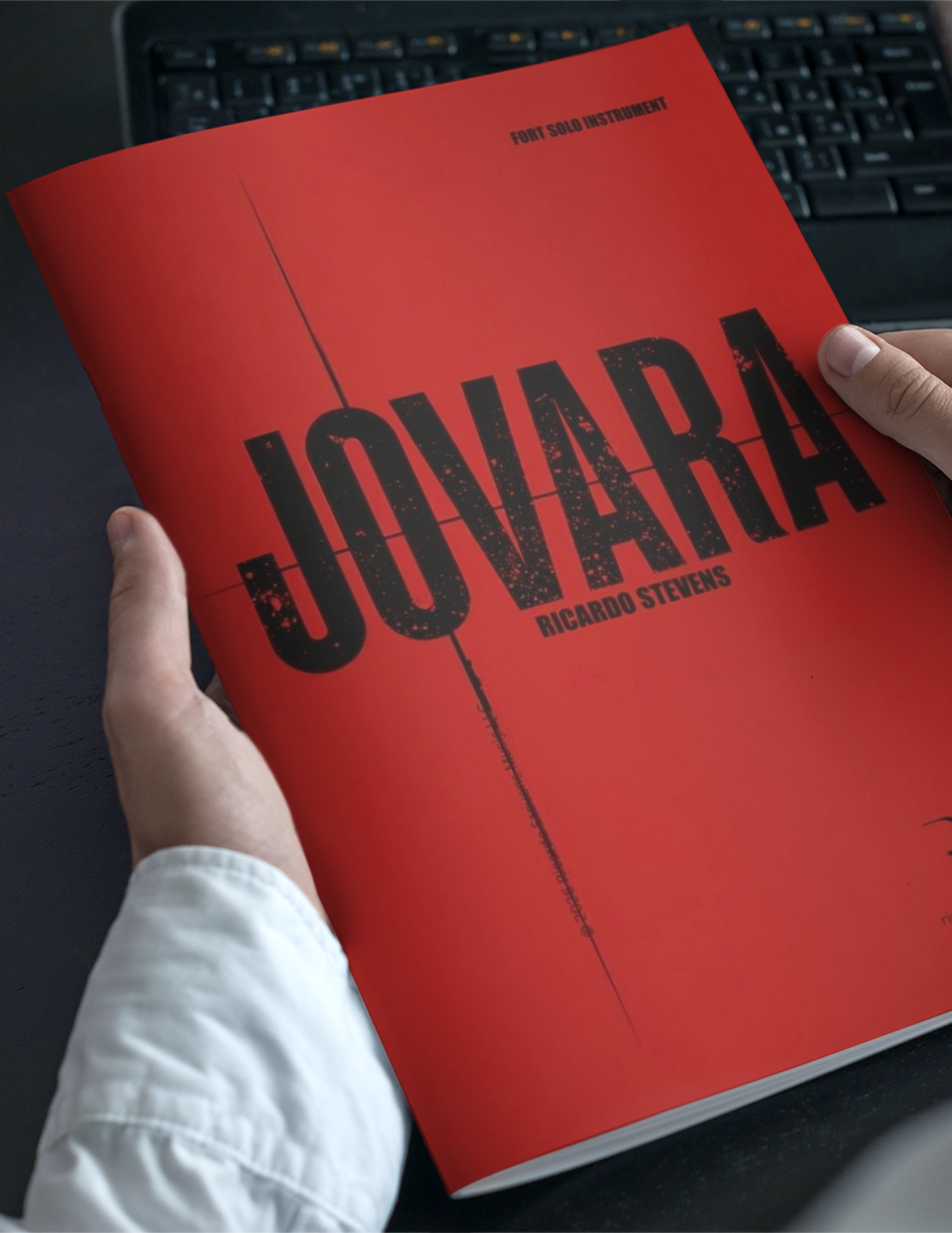 Red book titled 'Jovara' held by a person with a keyboard in the background by Ricardo Stevens